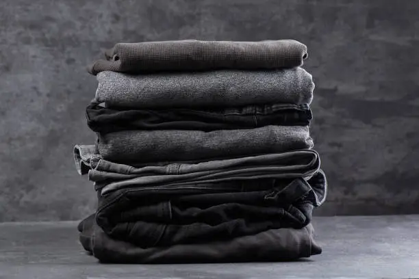 A stack of neatly folded dark clothes isolated on a black gray background close-up